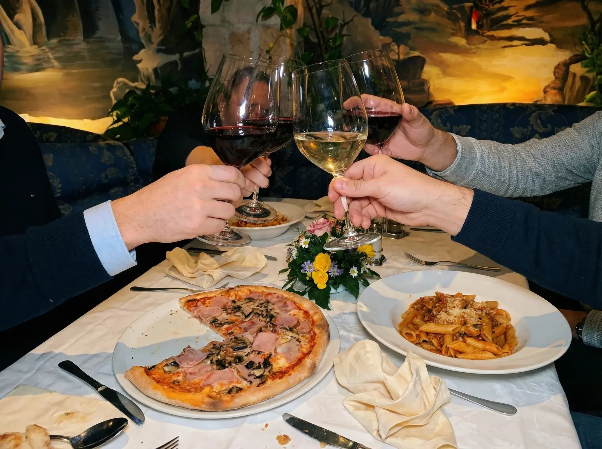 Mehrere Weingläser stoßen über Pizza und Pasta auf einen gemeinsamen Abend an.