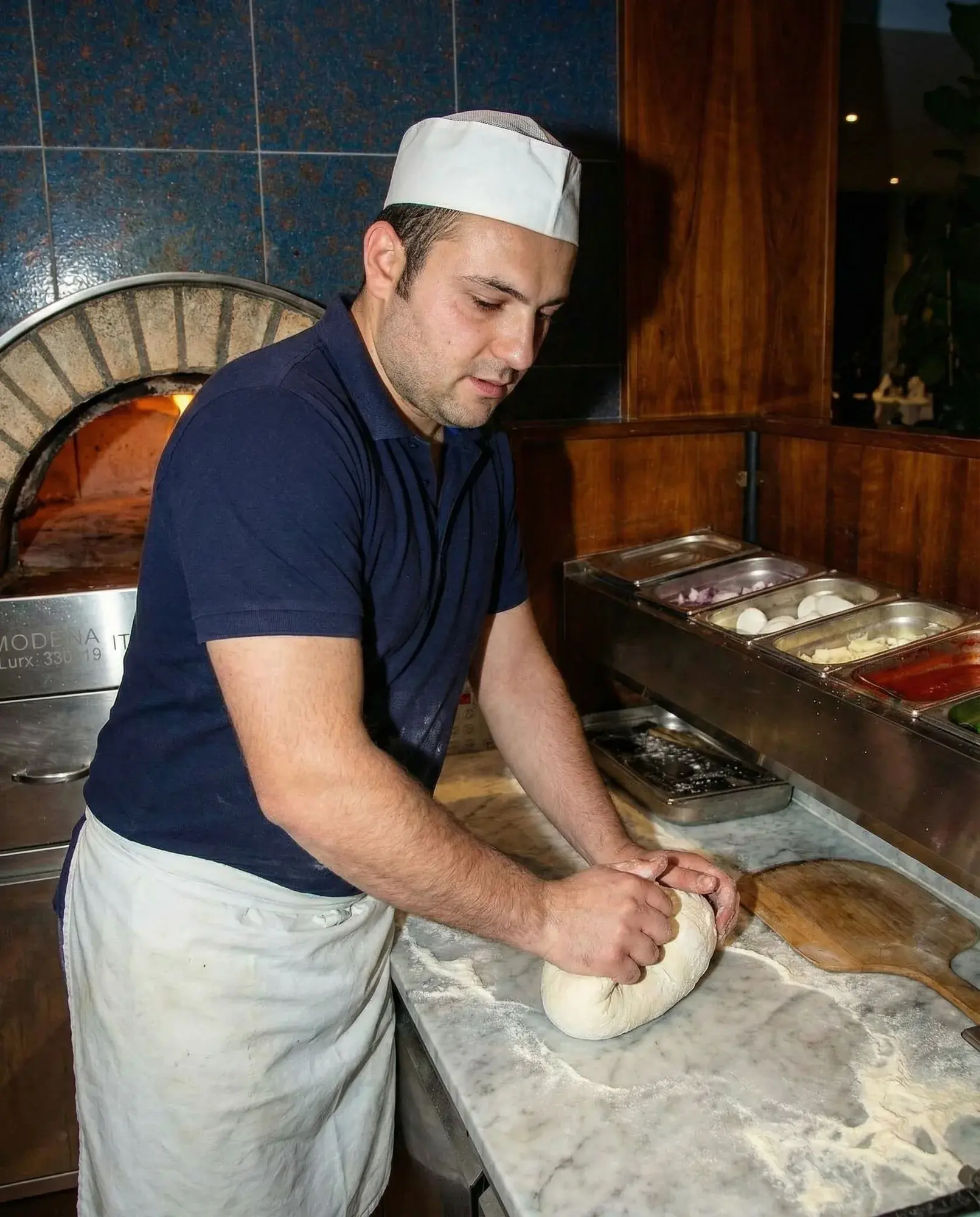 Pizzateig wird auf der bemehlten Arbeitsfläche geknetet.