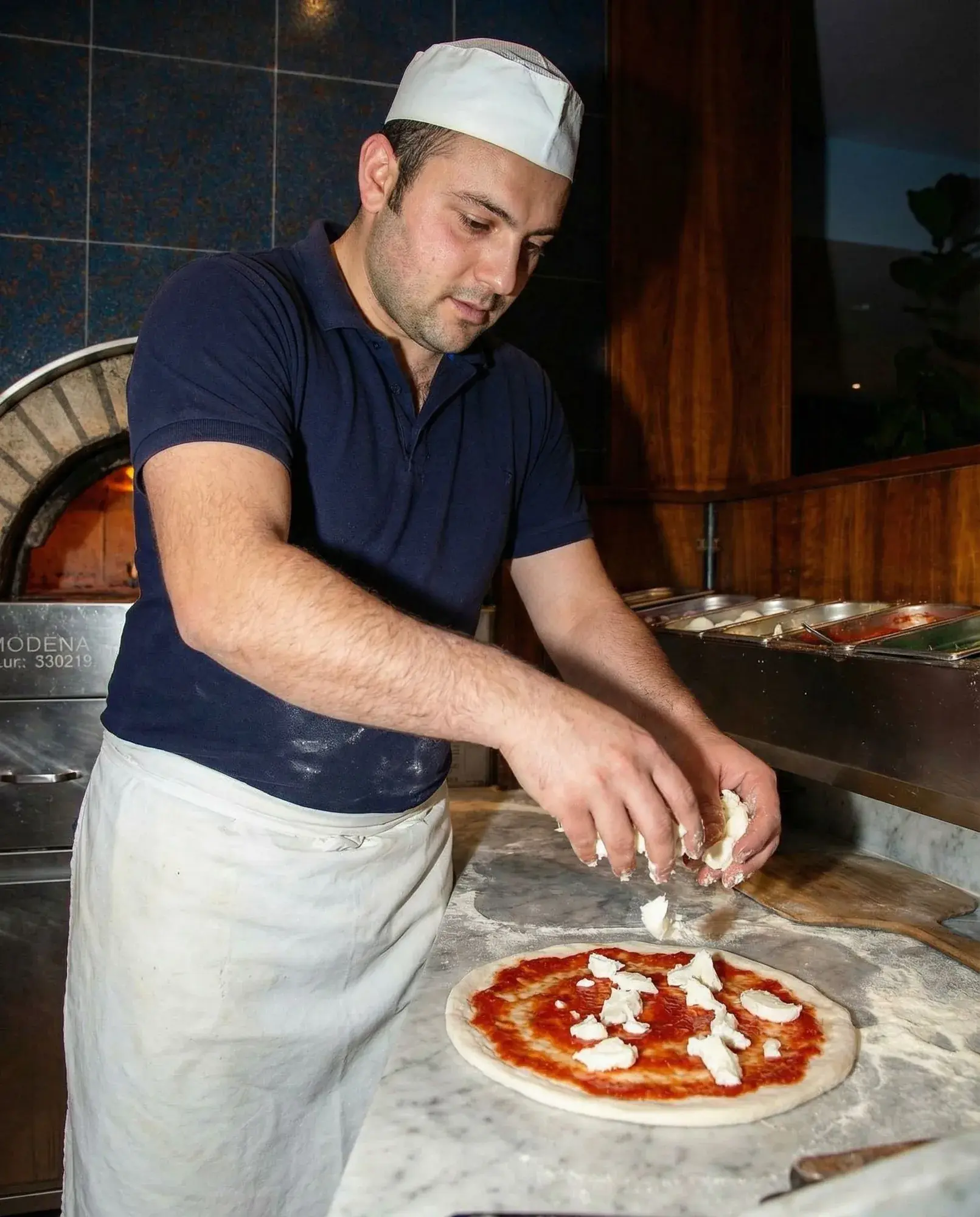 Mozzarella wird von Hand auf die Pizza verteilt.